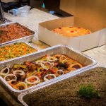 A selection of diverse dishes displayed in trays on a counter, showcasing an array of colors and textures.