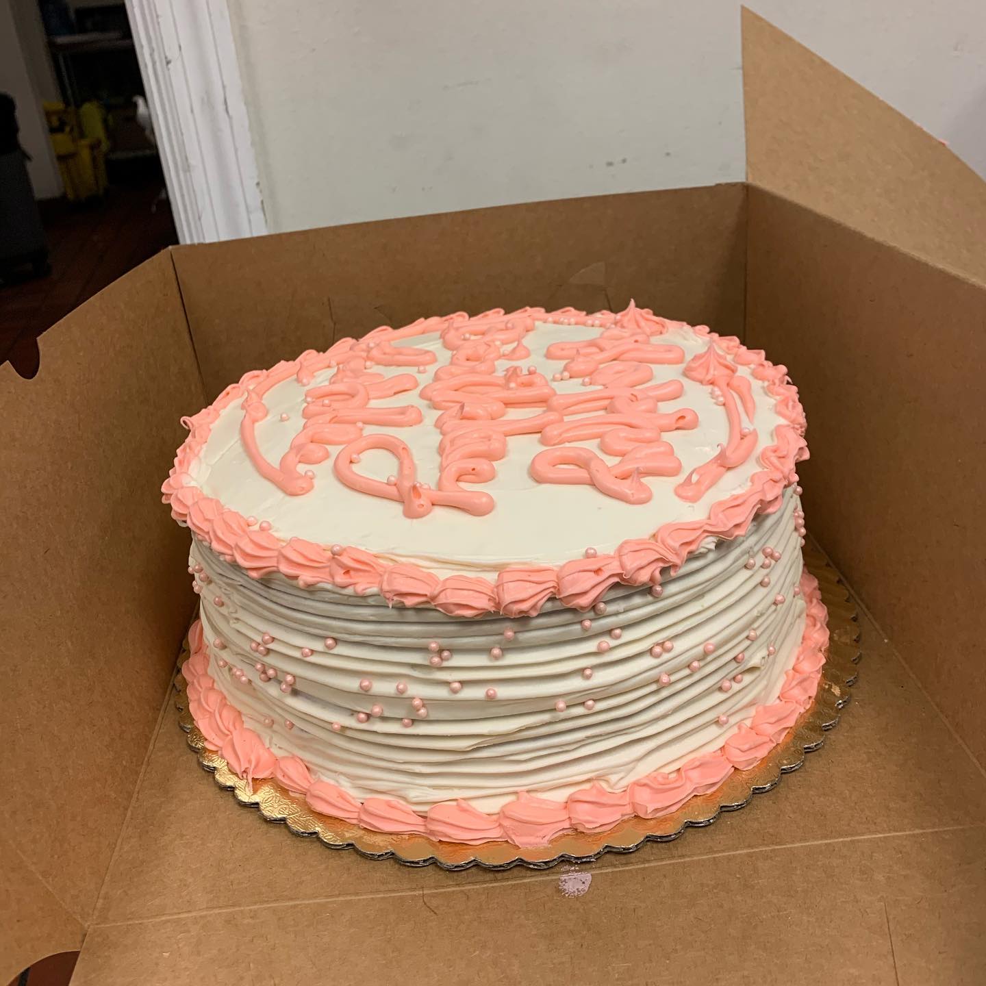 A cake with pink frosting displayed in a cardboard box, ready for celebration or gifting.