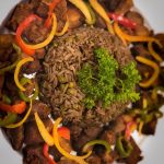 A plate featuring a serving of rice, Haitian food, and a colorful assortment of vegetables.