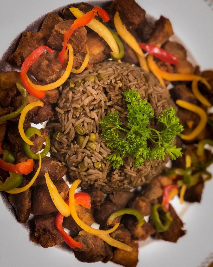 A plate featuring a serving of rice, Haitian food, and a colorful assortment of vegetables.