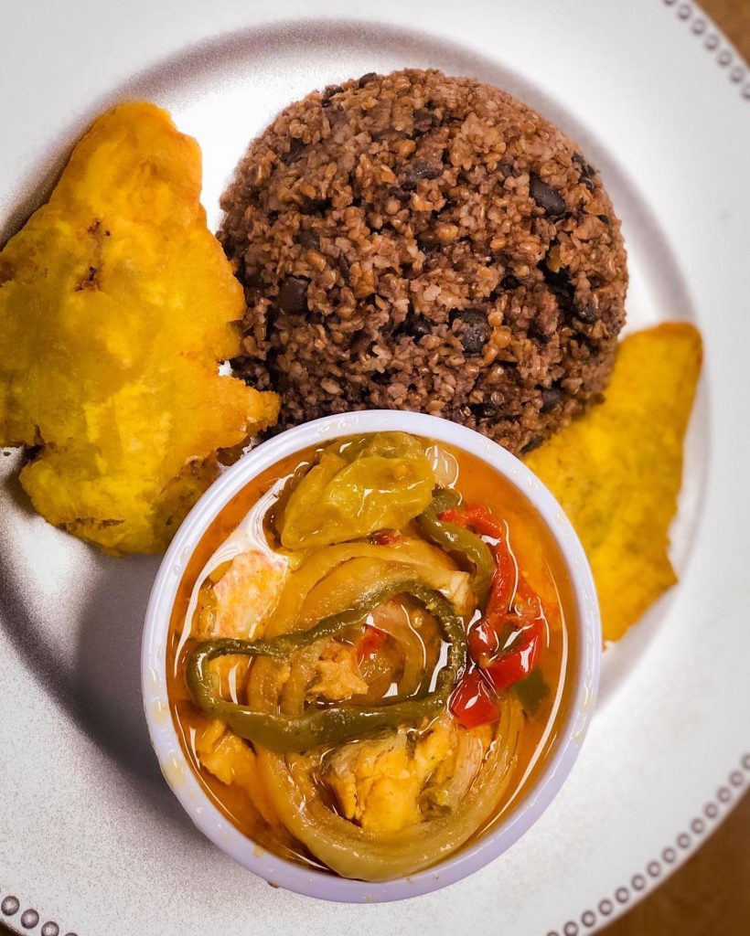 A white plate featuring a bowl filled with a colorful assortment of food.