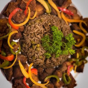 A plate featuring a serving of rice, Haitian food, and a colorful assortment of vegetables.